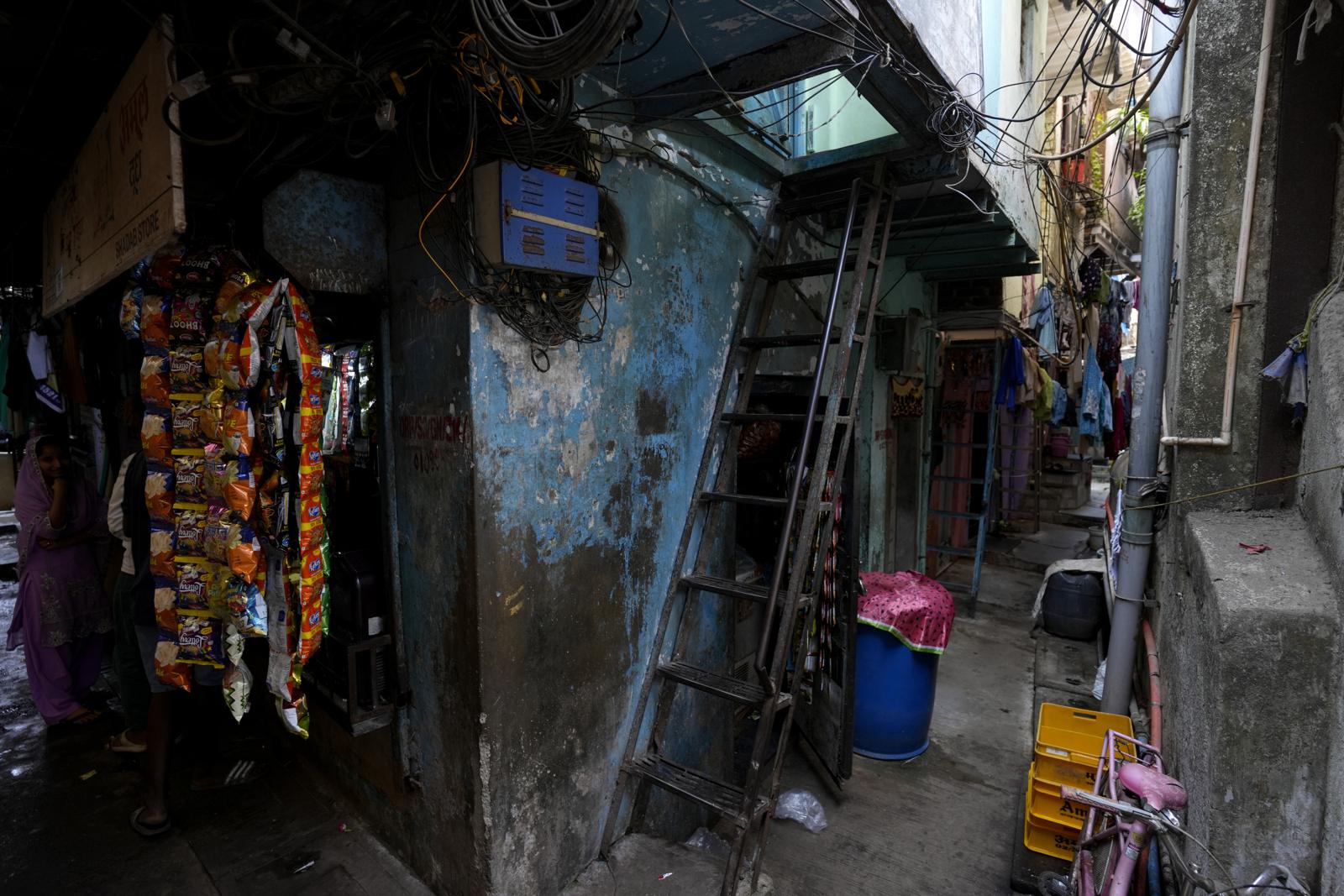 A narrow covered passage between houses in a settlement, with shops and a ladder to an upper room